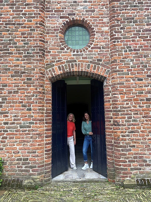 in de deuropening in de kerkmuur kijken Irmgard Admiraal en Chantal Huisstede om het hoekje